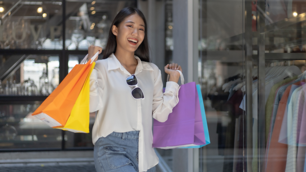 A person holding shopping bags in front of a store window.