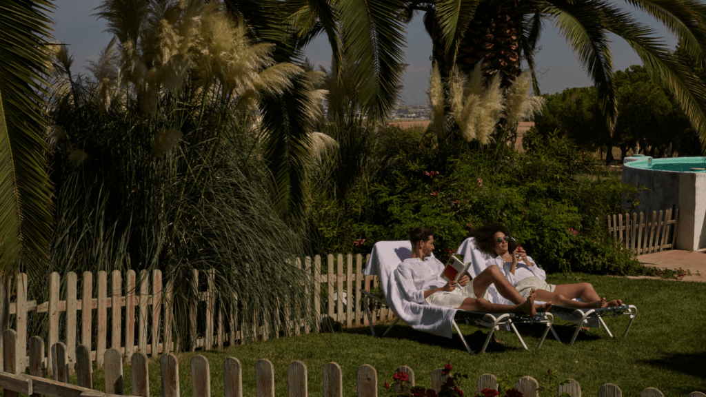 two people sitting in lawn chairs near a pool and palm trees