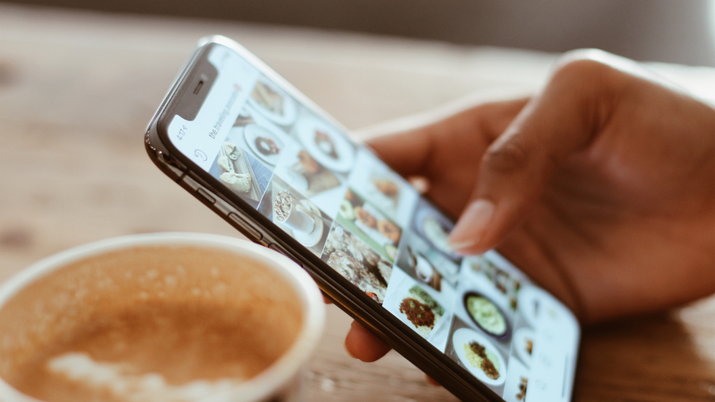 a person using an iphone and a cup of coffee on a wooden table