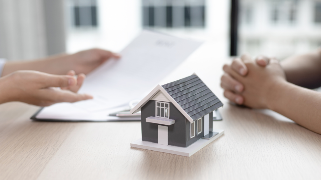 a person holding a house model and keys on a desk