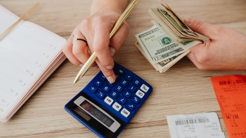 a person is counting money on a desk with a calculator and pen