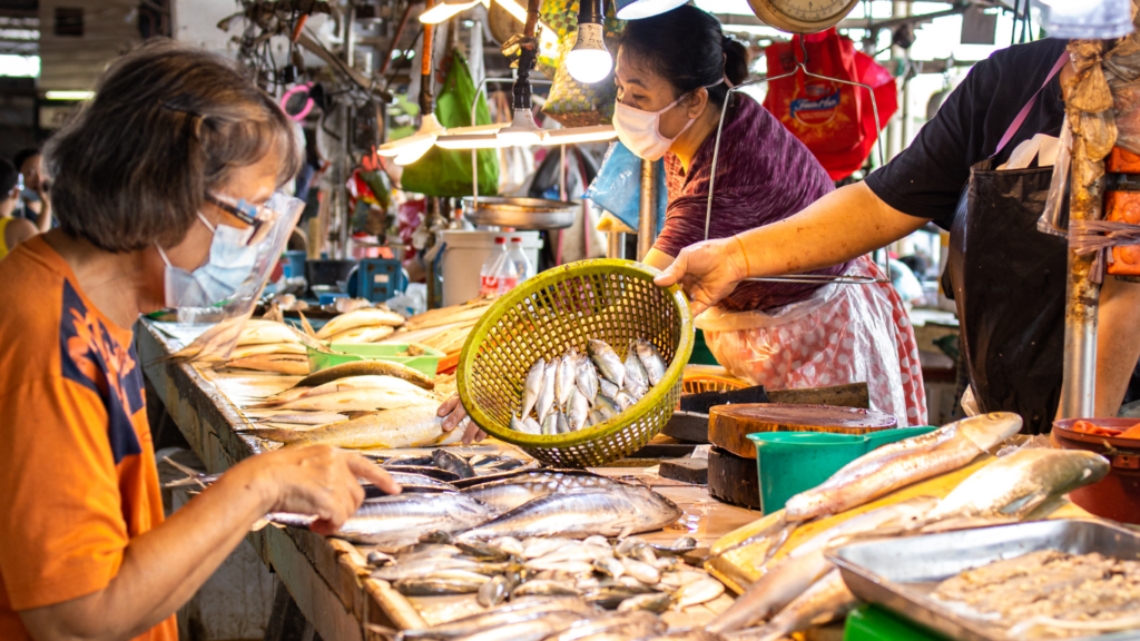 a person standing in front of meat and vegetables in a market